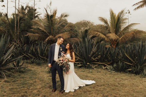 Bride and groom standing on grass walking in front of palm trees beach setting they look at each other