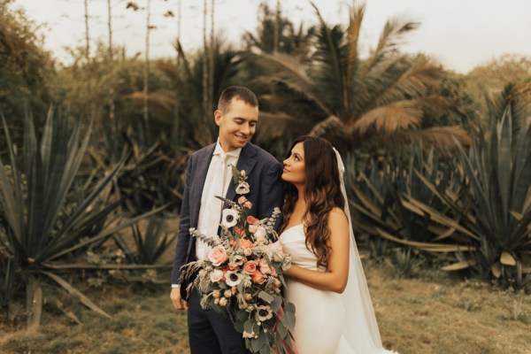 Bride and groom standing on grass walking in front of palm trees beach setting