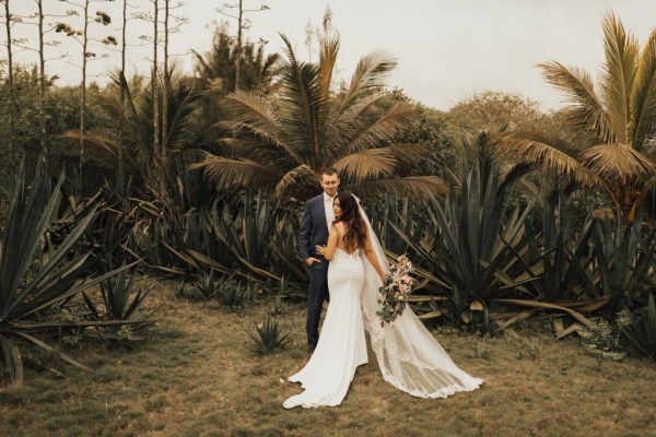 Bride and groom go in for a kiss palm trees in background bouquet behind brides back