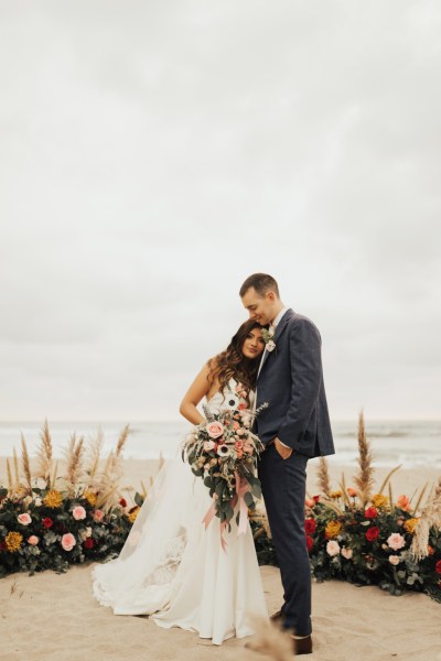 Bride and groom beach setting hugging bouquet in shot