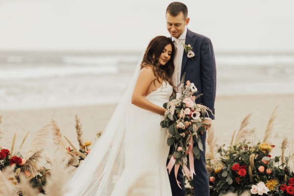 Bride and groom beach setting hugging bouquet in shot