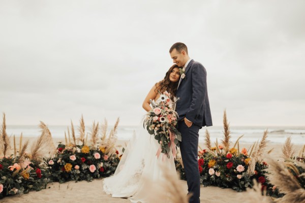 Bride and groom beach setting hugging bouquet in shot