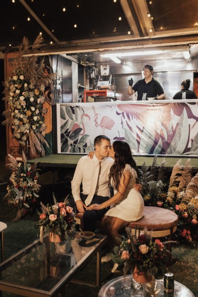 Bride and groom sitting in front of DJ booth facing each other they go in for a kiss