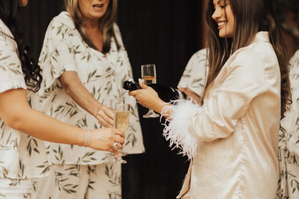 Bride and her bridesmaids in loungewear bridalwear opening bottle of champagne