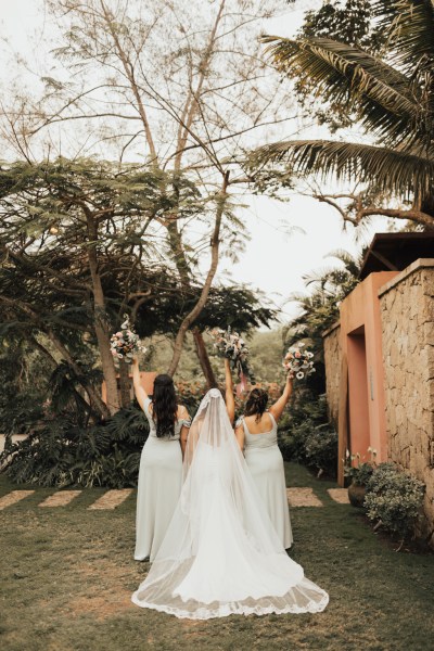 Bride and her bridesmaids standing with bouquet/flowers garden setting from behind flowers in the air