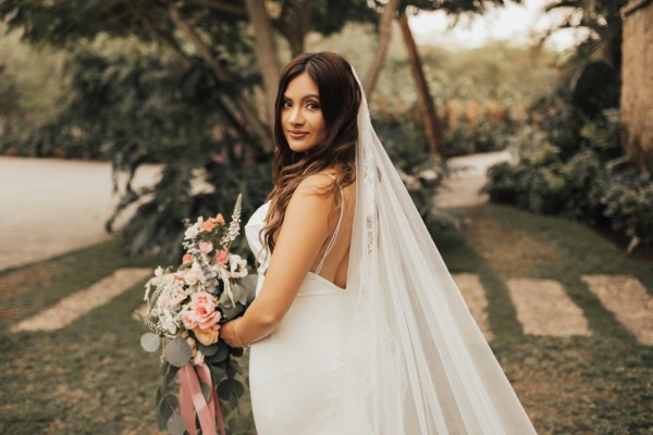 Bride standing in garden holding bouquet side view