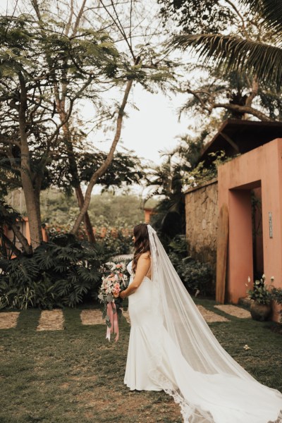 Bride standing in garden holding bouquet she looks away