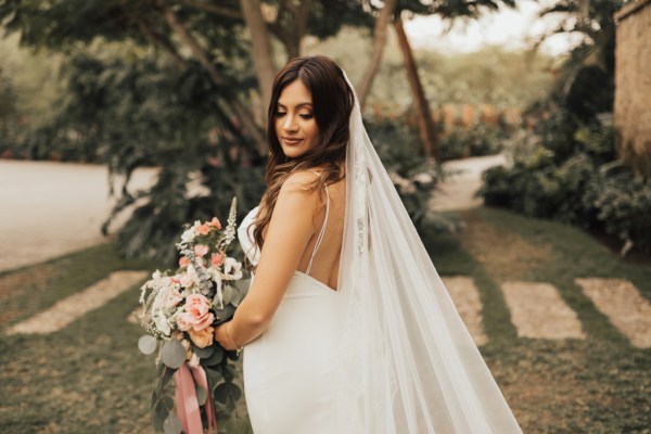 Bride standing in garden holding bouquet looking down