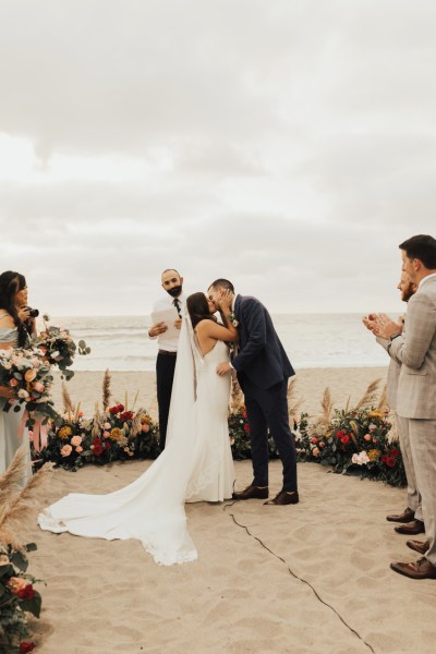 Bride groom and celebrant beach setting and guests standing sea in background