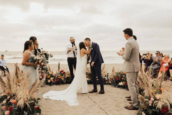 Bride groom and celebrant beach setting and guests standing sea in background