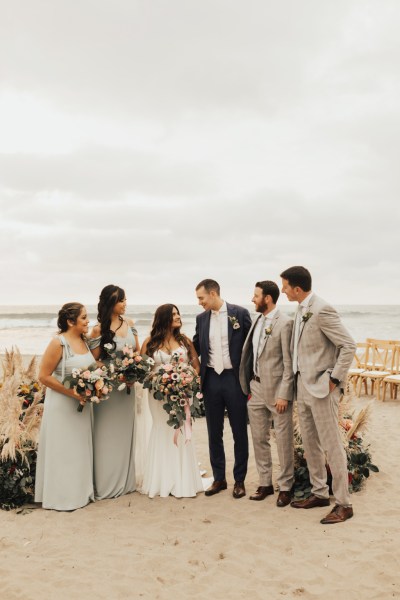 Bride and groom bridesmaids and groomsmen pose for a picture beach setting