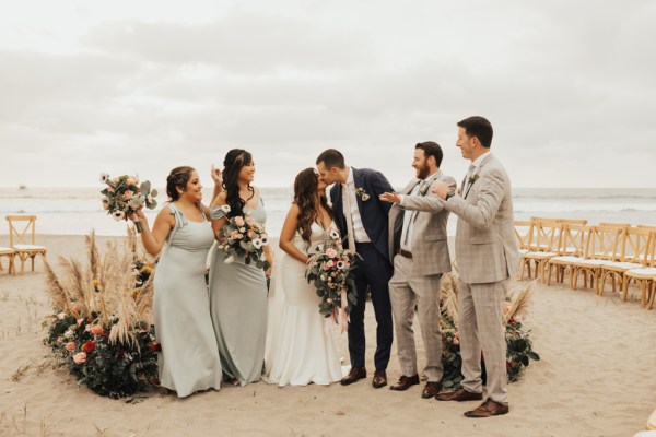 Bride and groom bridesmaids and groomsmen pose for a picture beach setting they kiss