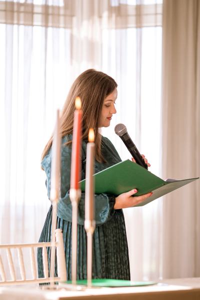 Celebrant wearing green speaks into microphone candles lit