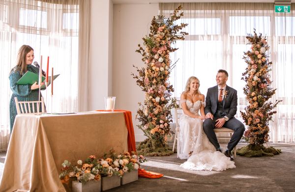 Bride and groom sit at the alter during ceremony surrounded by flowers