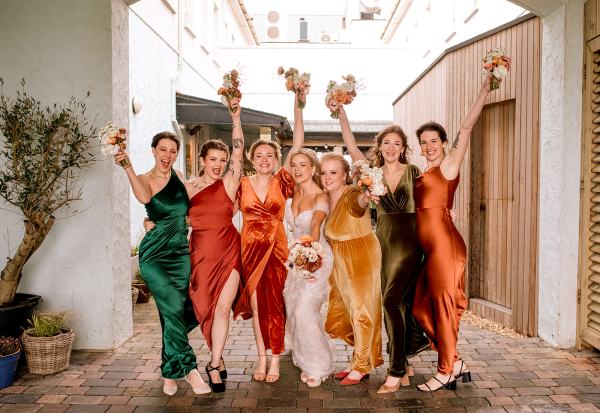 Bride bridesmaids and friends pose for a photo holding bouquet in the air