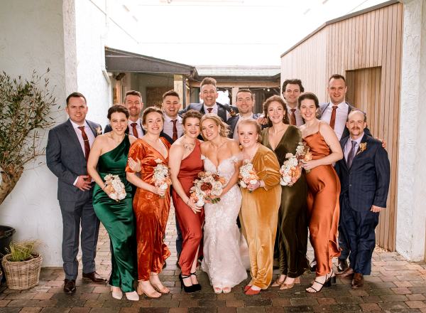 Bride bridesmaids and friends pose for a photo holding bouquet and men