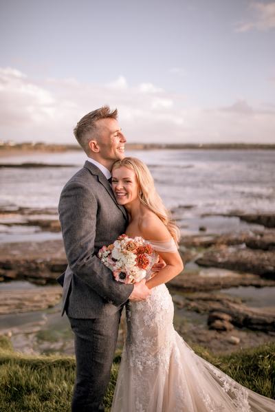 Bride and groom pose in front of beach ocean sea view setting smiling