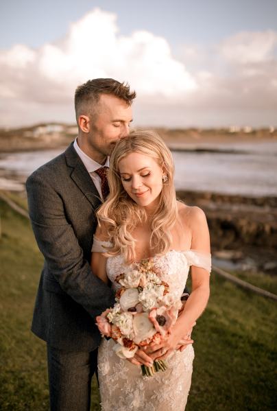 shot of bride and groom ocean in background smiling kiss on the head bride looks down