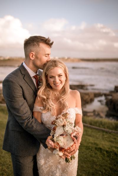 shot of bride and groom ocean in background smiling kiss on the head