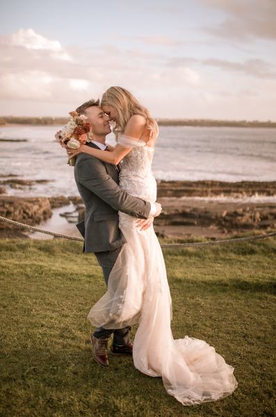 Groom picks up bride beach setting bouquet in shot grass