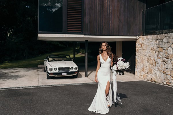 Grace Loves Lace: Jones Dress facing camera holding bouquet flowers wearing bridal gown with slit down the leg poses