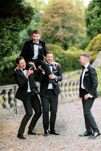 Groomsmen and groom joke around they put groom on shoulders lift him up