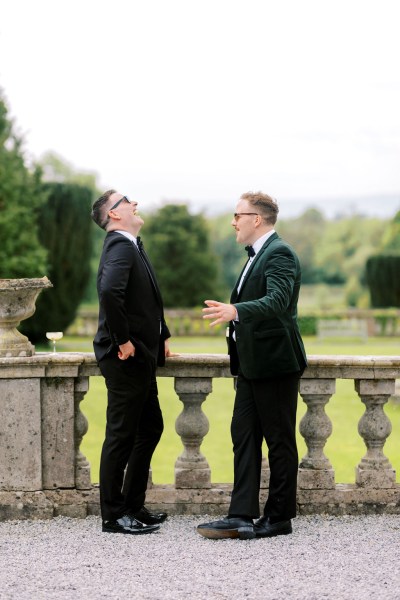 Two men standing at balcony ledge overlooking garden