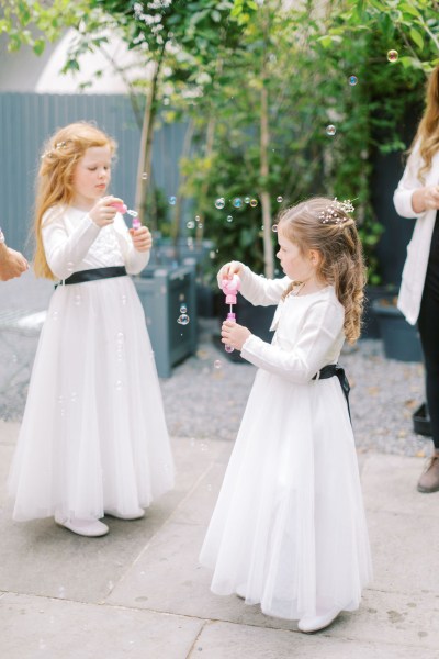 Two little girls in white dresses blowing bubbles