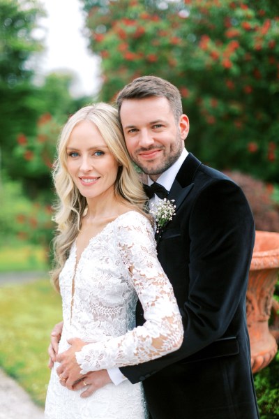 groom has arms around brides waist they face the camera