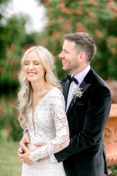 groom has arms around brides waist they're laughing