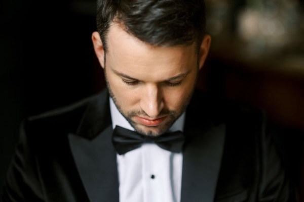 Groom looks down wearing bowtie shirt and suit