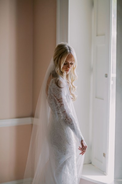 Bride looks down wearing veil facing window