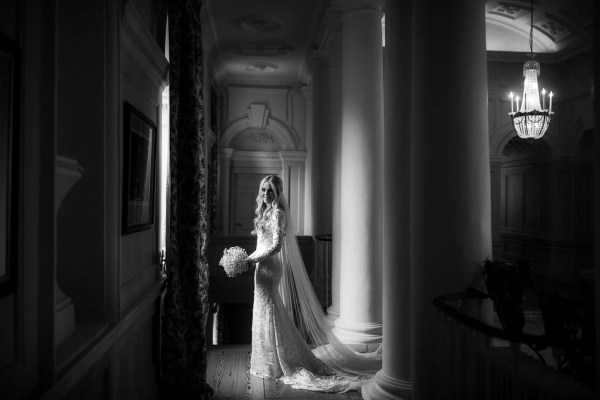 Black and white bride stands in corridor beside pillars holding bouquet