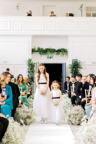 Two flower girls wearing white dresses walk down the aisle