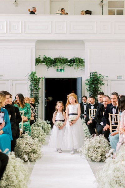 Two flower girls wearing white dresses walk down the aisle