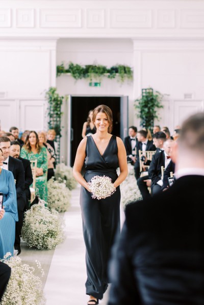 Bridesmaid in black dress walks down the aisle