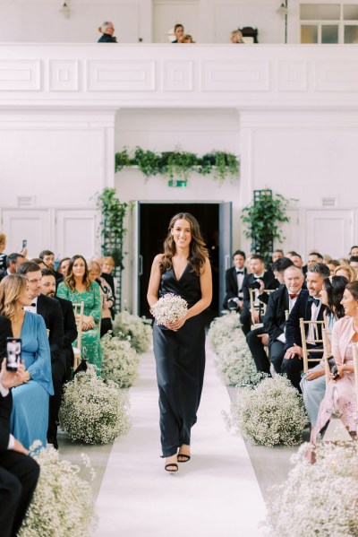 Bridesmaid in black dress walks down the aisle