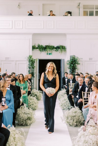 Bridesmaid in black dress walks down the aisle