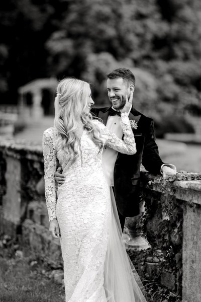 Bride places hand on grooms face over the shoulder shot black and white