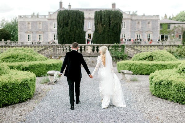 Bride and groom from behind walking along pathway to garden