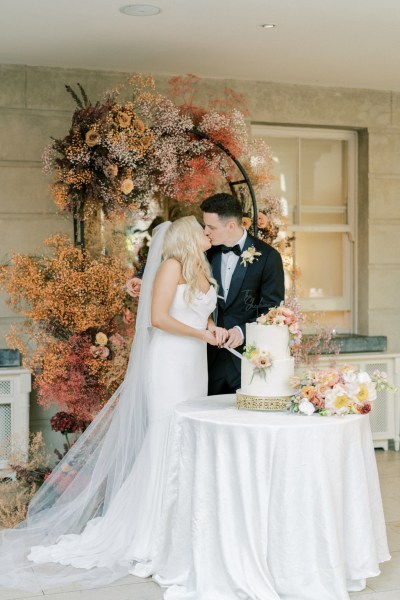 Bride and groom kiss kissing as they cut the white wedding cake