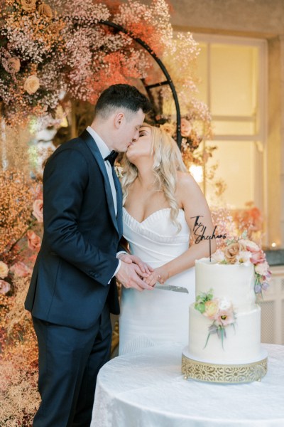 Bride and groom kiss kissing as they cut the wedding cake