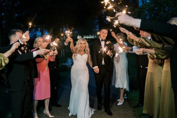 Groom leans hold sparklers and guests hold up sparklers in background