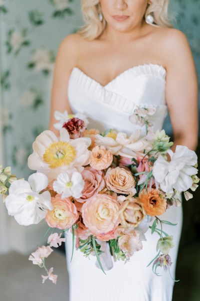 Bride standing on her own in room holding bouquet looking down