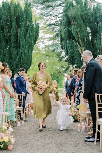 Bridesmaids and little girl in white dress walk down the aisle