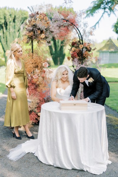 Bride and groom sign marriage certificate at white table