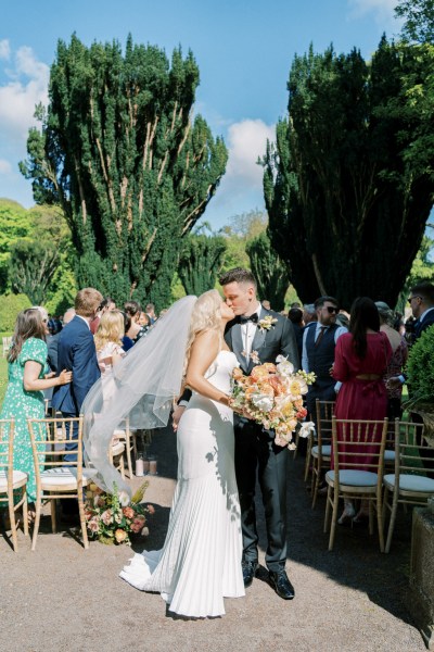 Bride and groom exit wedding ceremony as guests clap they kiss