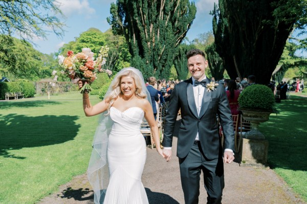 Bride and groom exit wedding ceremony as guests clap they walk along pathway