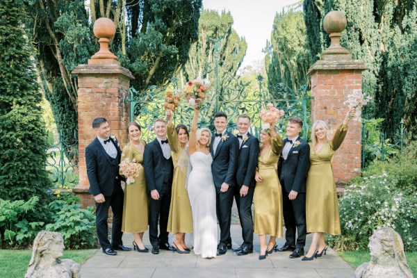 Bride groom groomsmen and bridesmaid pose outside wedding venue pillar gates