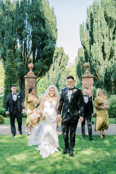 Bride and groom walk on the grass followed by bridesmaids and groomsmen